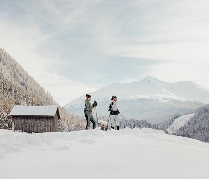 Two people cross-country skiing in snowy mountain valley with huts in background
