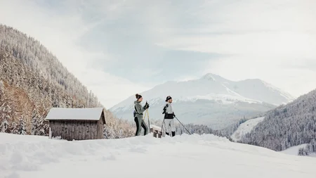 Two people cross-country skiing in snowy mountain valley with huts in background