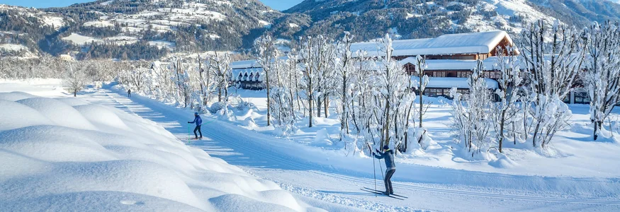 Dolomitengolf Hotel & Spa ****S © Martin Lugger Menschen beim Langlaufen auf schneebedecktem Weg vor Bergkulisse