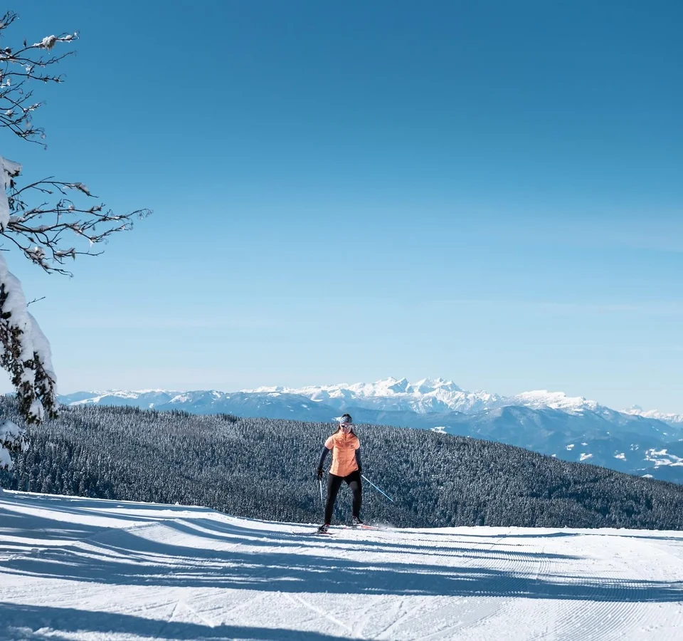 Slow Down in Slowenien © Daniel Hug Person beim Skilanglauf vor schneebedeckten Bergen und blauem Himmel