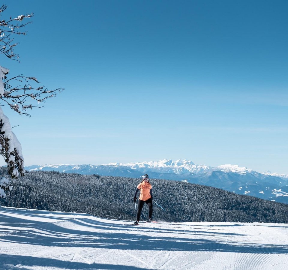 Slow Down in Slowenien © Daniel Hug Person beim Skilanglauf vor schneebedeckten Bergen und blauem Himmel