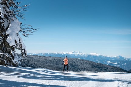 Person beim Skilanglauf vor schneebedeckten Bergen und blauem Himmel
