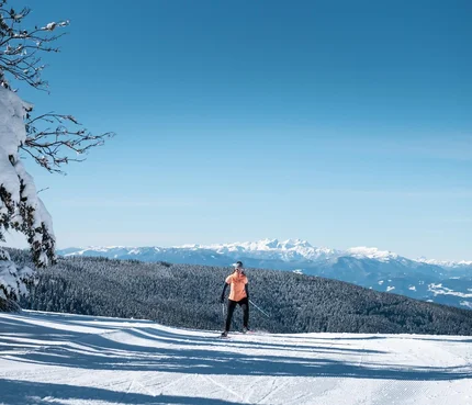 Person beim Skilanglauf vor schneebedeckten Bergen und blauem Himmel