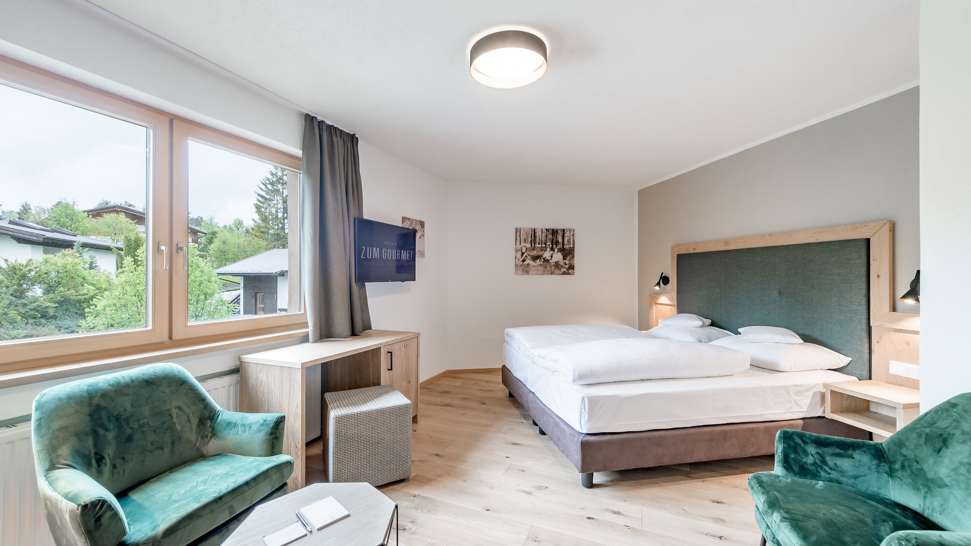 Bright hotel room with double bed and green armchairs