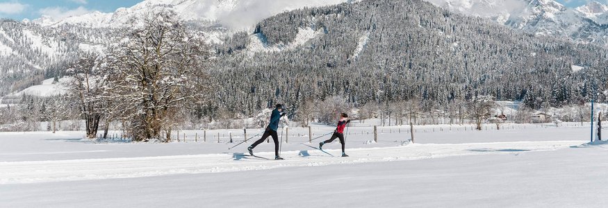 Zwei Langläufer in verschneiter Landschaft mit Bergen im Hintergrund