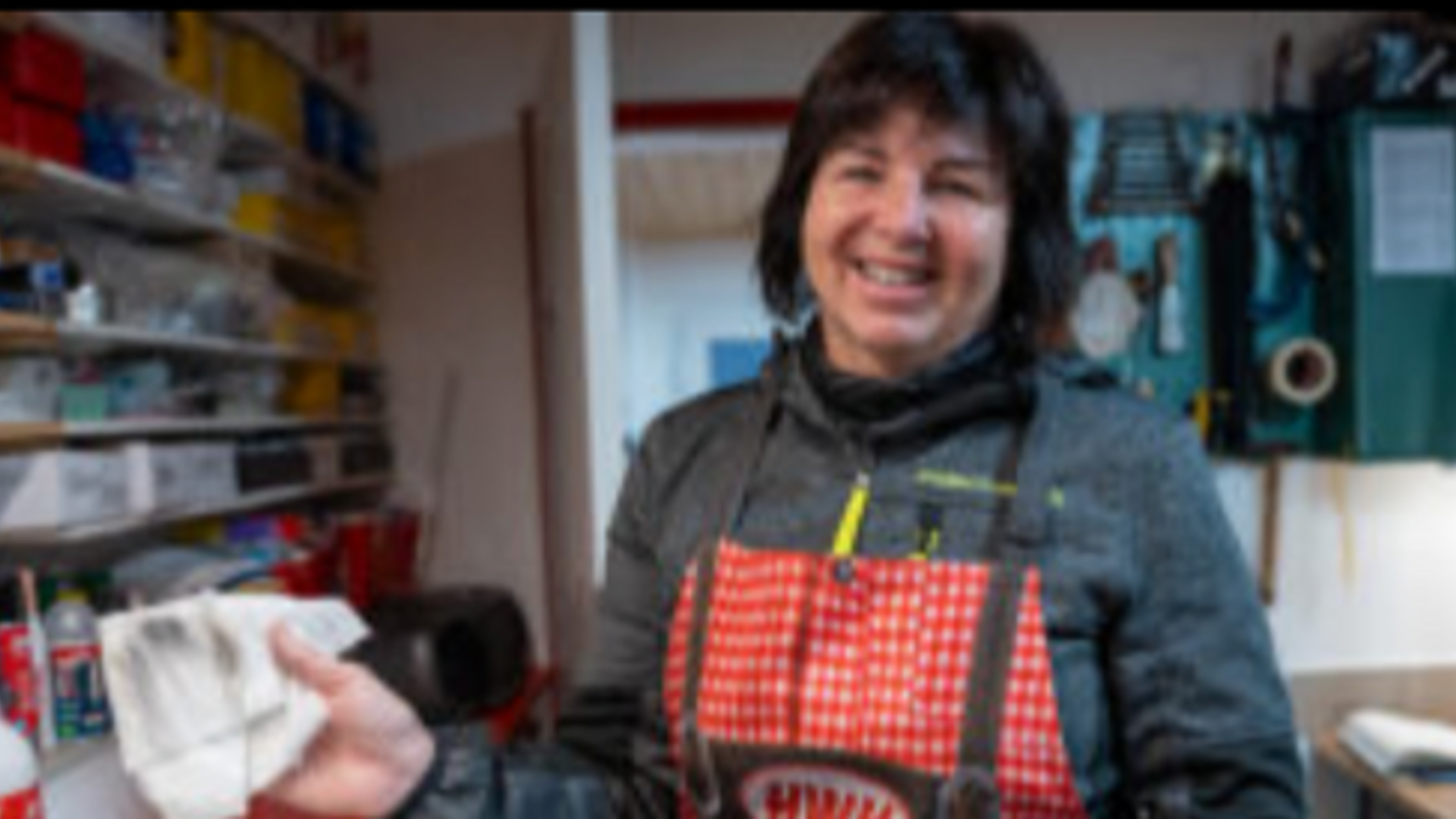 Frau in Werkstatt trägt Schürze und hält Tuch in der Hand