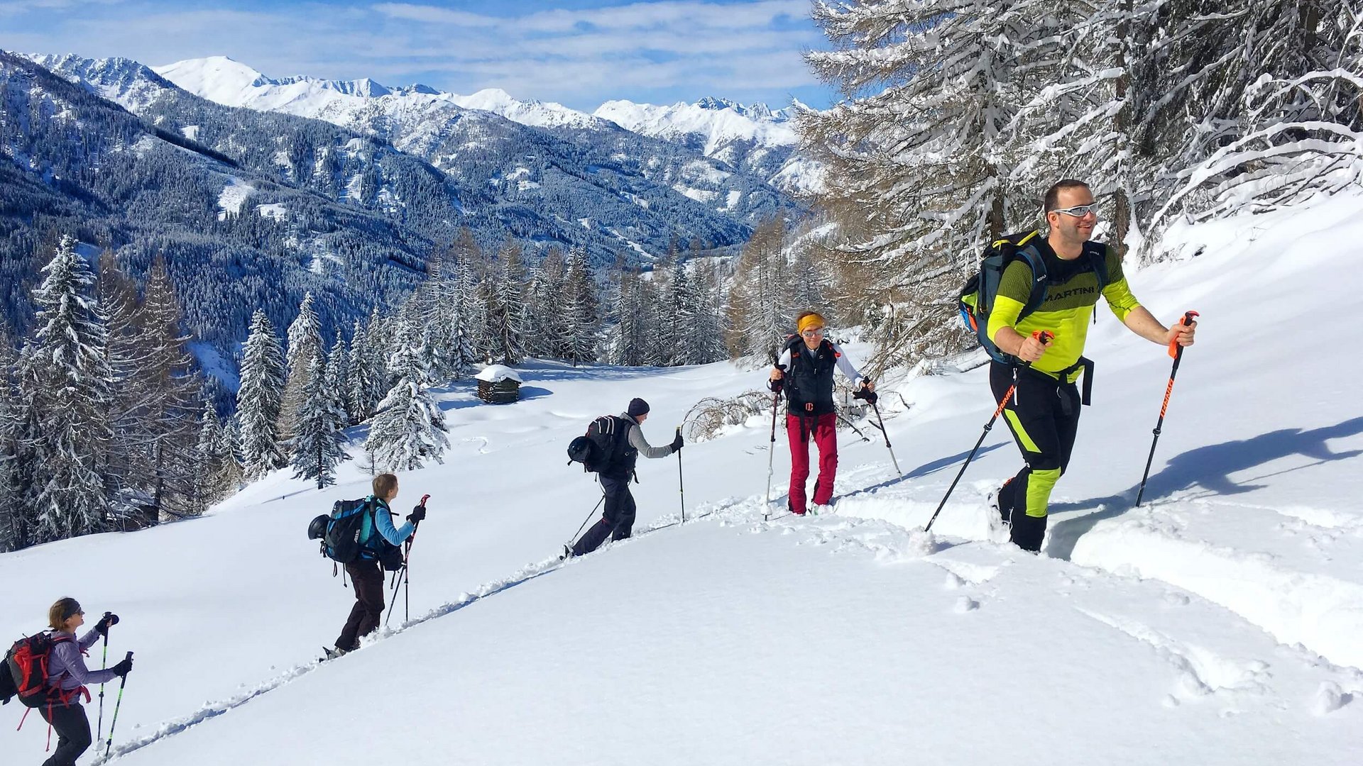 Group snowshoe hiking in snowy mountain landscape under clear blue sky