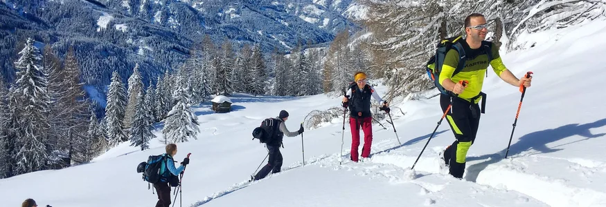Gruppe beim Schneeschuhwandern in verschneiter Berglandschaft unter blauem Himmel