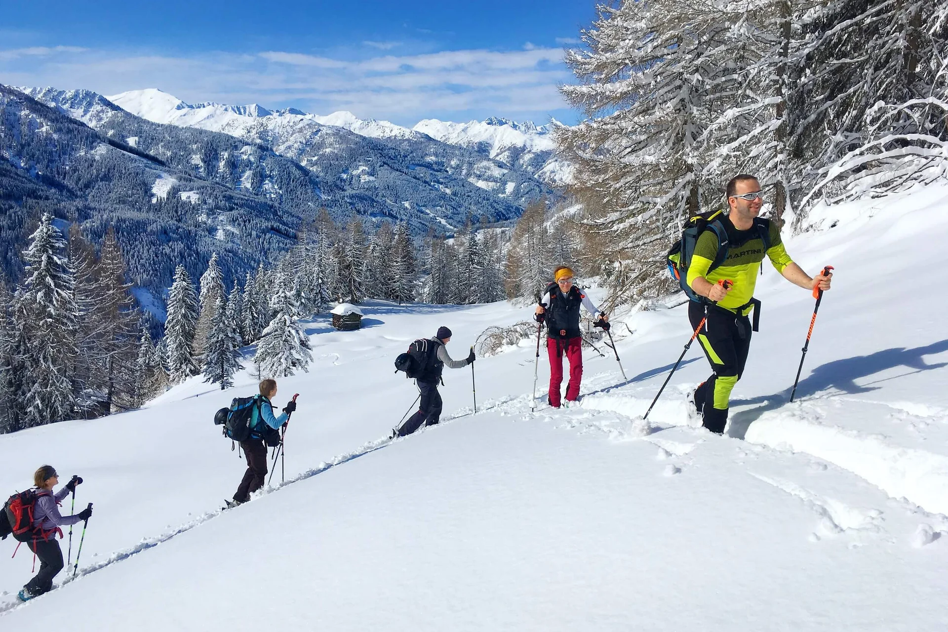 Gruppe beim Schneeschuhwandern in verschneiter Berglandschaft unter blauem Himmel