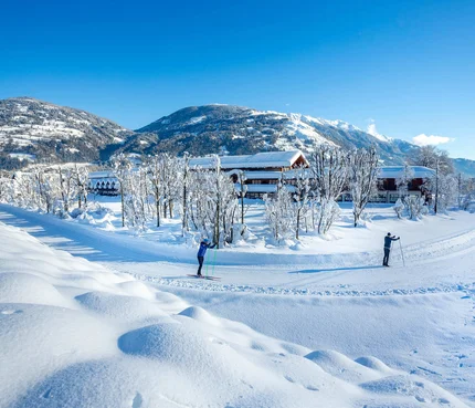 Two skiers on snowy trail with mountains and houses in background
