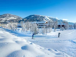 Two skiers on snowy trail with mountains and houses in background