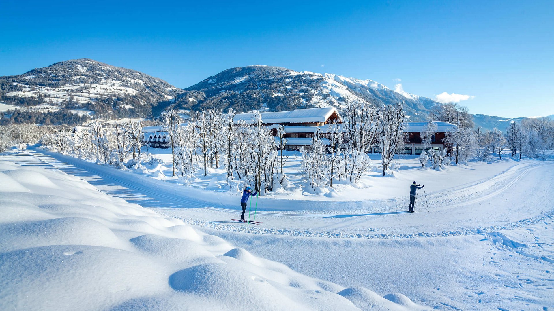 Zwei Skifahrer auf verschneiter Loipen vor Berglandschaft und Häusern