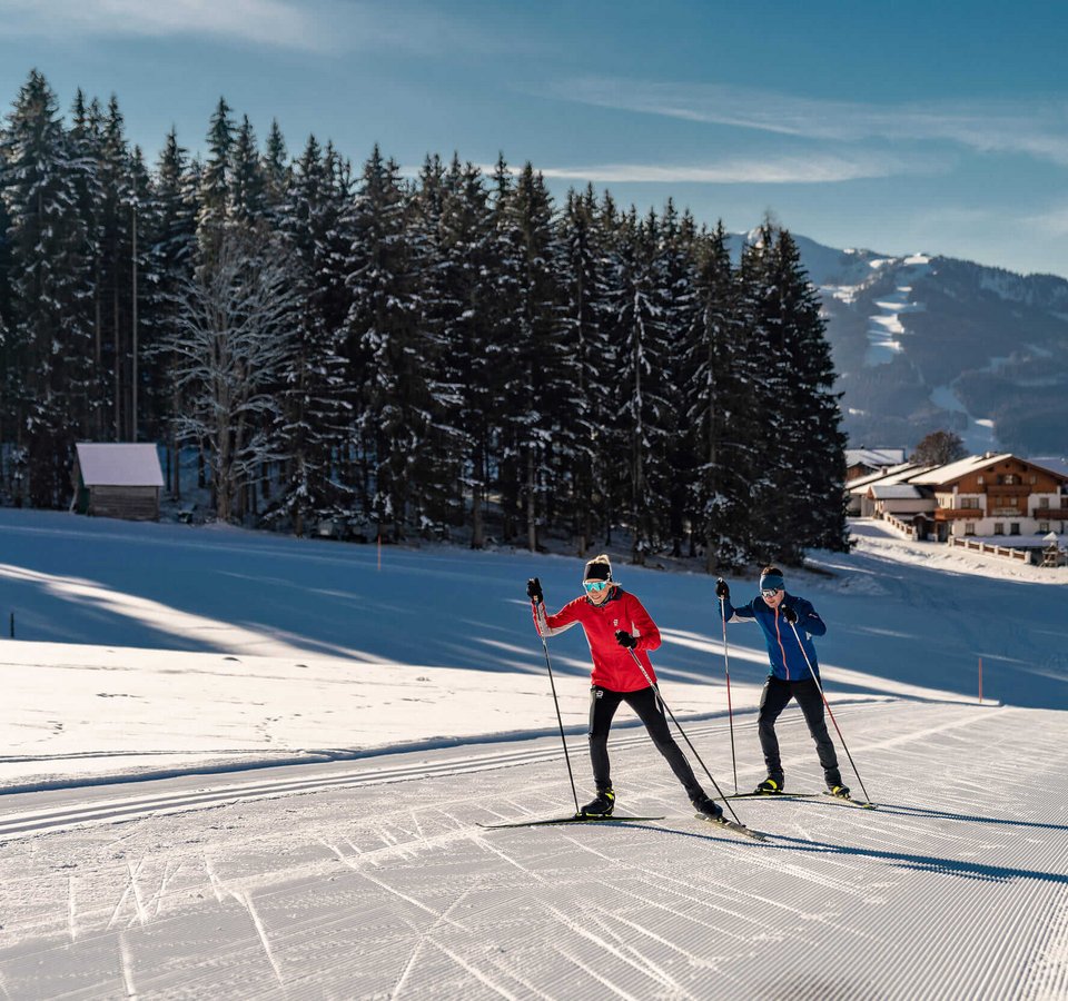 Fis Weltcup Nordische Kombination © TVB Schladming Dachstein - Christine Höflehner Zwei Langläufer auf verschneiter Loipe vor Wald und Bergen