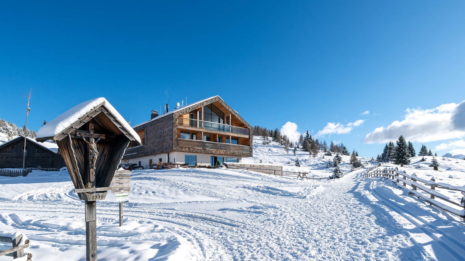 Schneebedecktes Berghaus mit Winterweg und hölzernem Kreuz in den Alpen