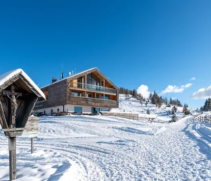 Schneebedecktes Berghaus mit Winterweg und hölzernem Kreuz in den Alpen