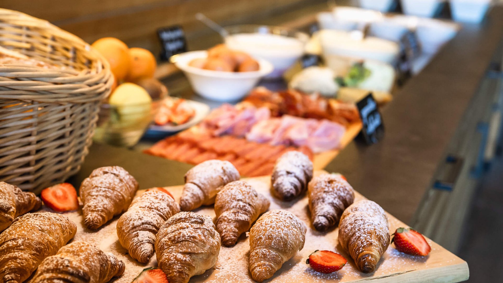 Croissants mit Puderzucker und Erdbeeren auf einem Buffet mit Wurst und Obst