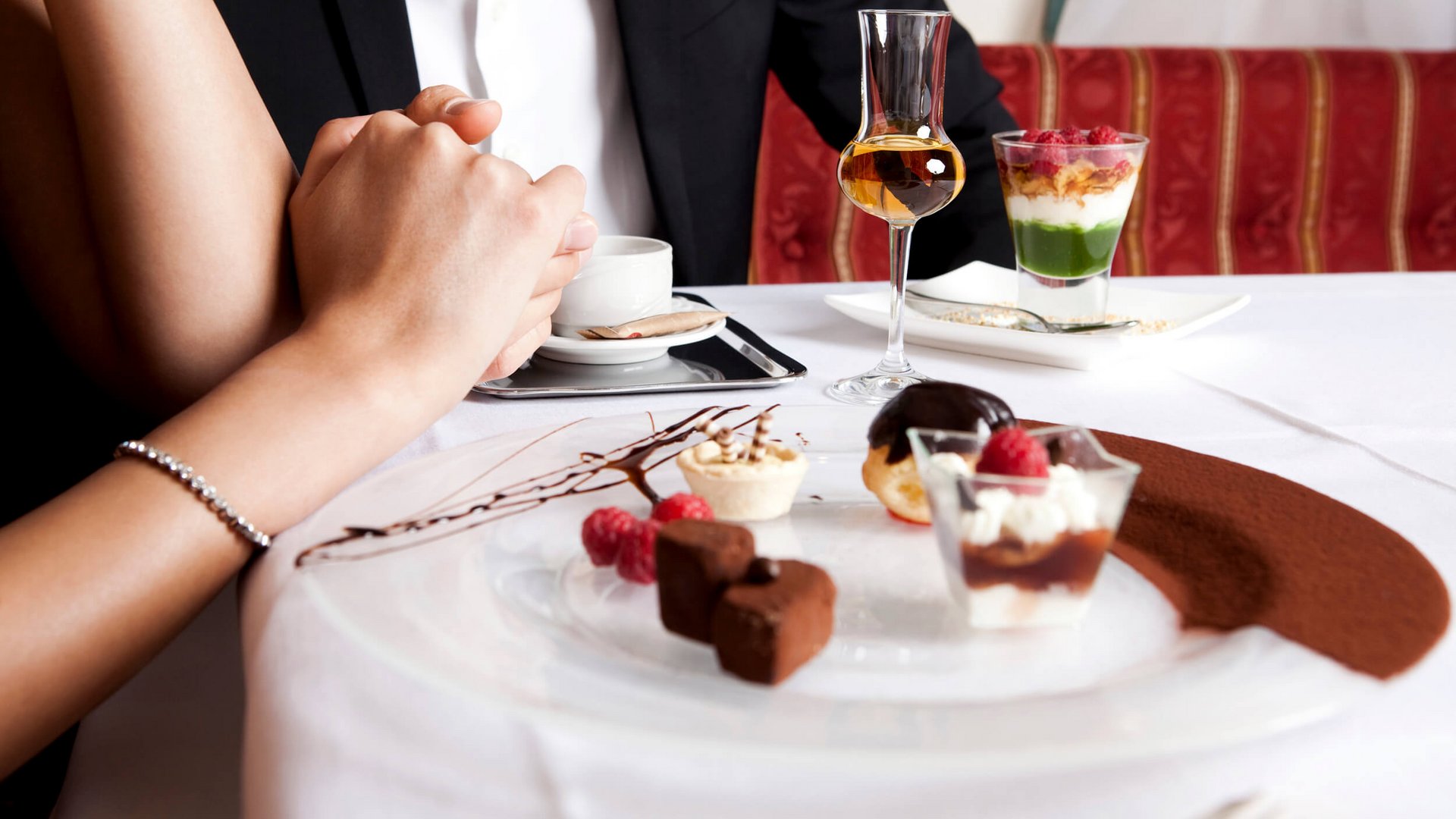 Paar hält Hände an einem Tisch mit einem Dessert und einem Glas Likör