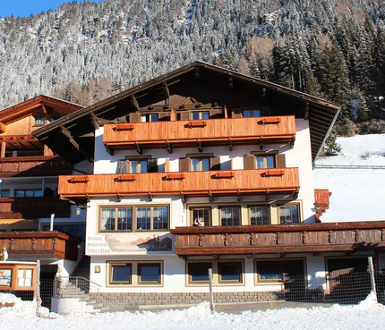 Alpenhaus mit verschneiten Bäumen im Hintergrund unter blauem Himmel