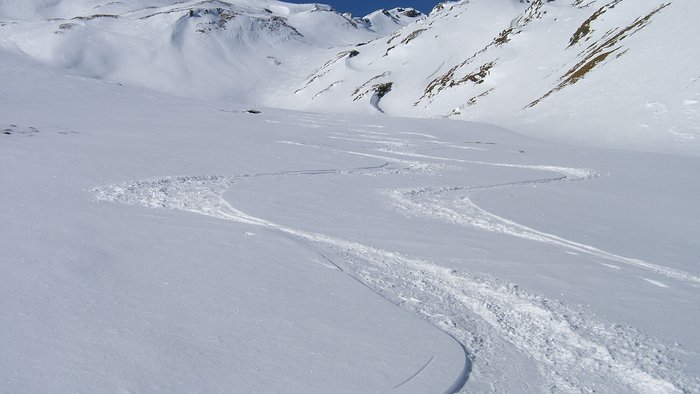 Spuren von Skifahrern im unberührten Schnee an einem sonnigen Berghang