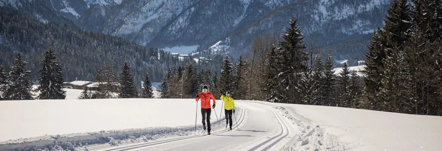 PillerseeTal © Mirja Geh Two cross-country skiers on snowy trail with mountains in the background