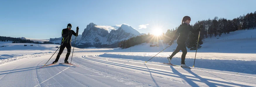 Two people cross-country skiing in a snowy mountain landscape at sunrise