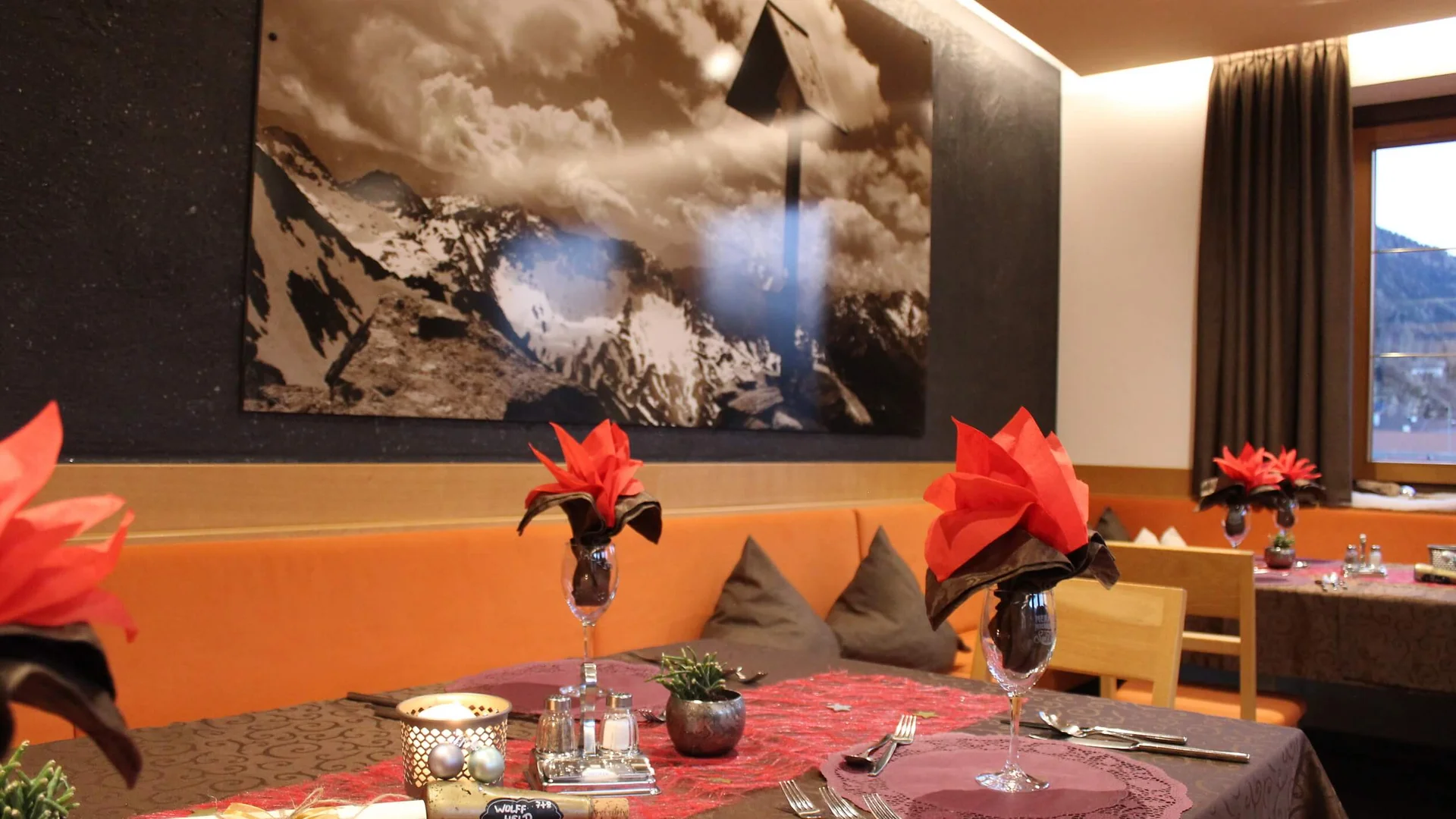 Gemütlicher Restauranttisch mit roten Servietten und Bergbild an der Wand
