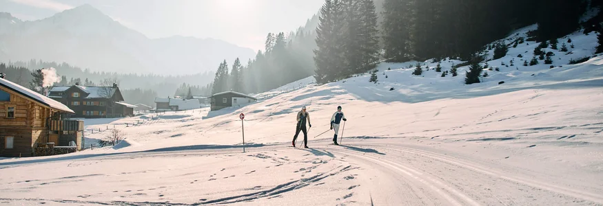 Genuss- und Aktivhotel Sonnenburg **** © Kleinwalsertal Tourismus - Oliver Farys Zwei Langläufer auf einer verschneiten Loipe vor Wald und Bergen