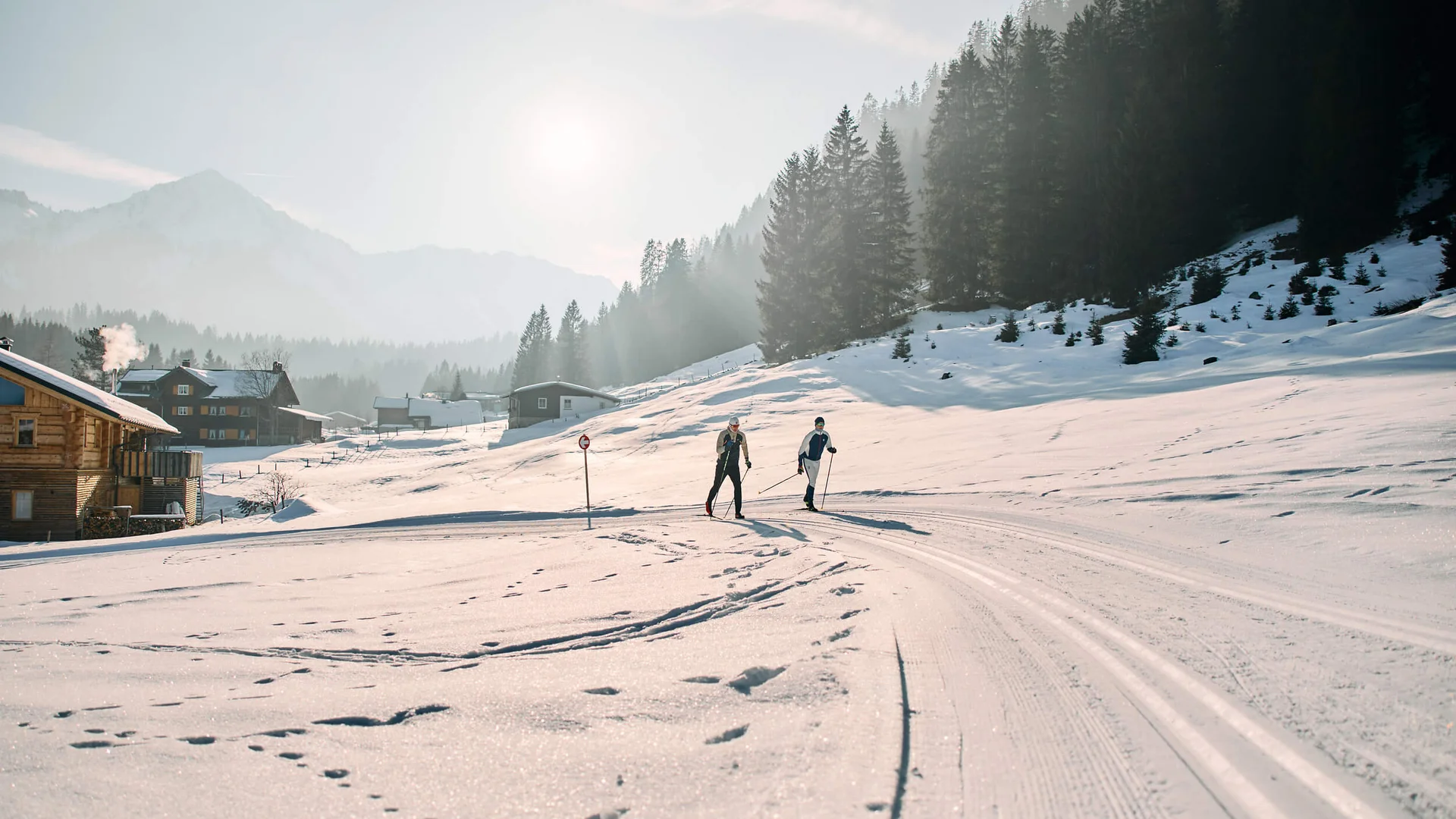 Langlauf Urlaub im Kleinwalsertal © Kleinwalsertal Tourismus - Oliver Farys Zwei Langläufer auf einer verschneiten Loipe vor Wald und Bergen