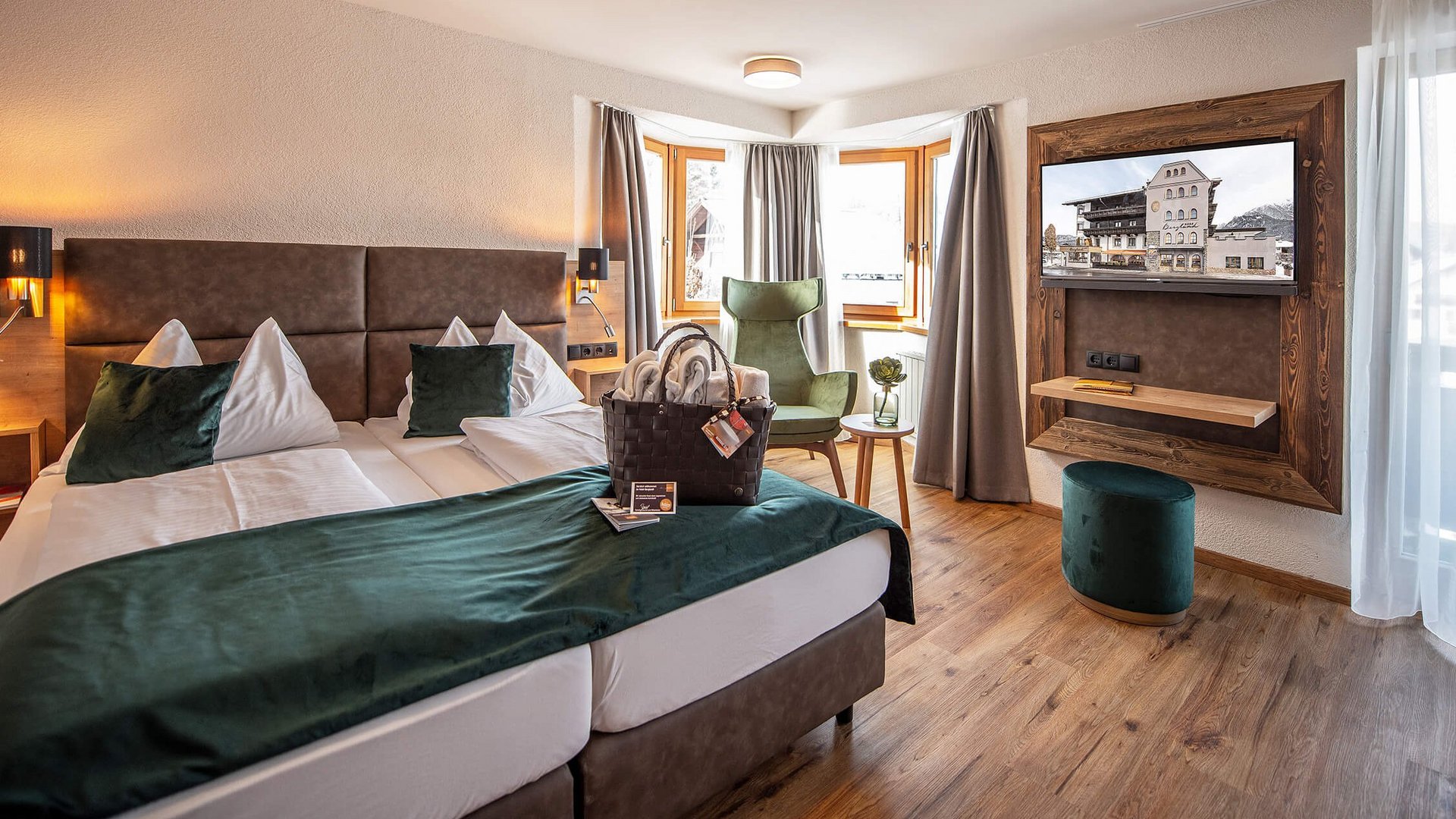 Gemütliches Hotelzimmer mit zwei Betten, Sesseln und Fernseher vor Fensterfront