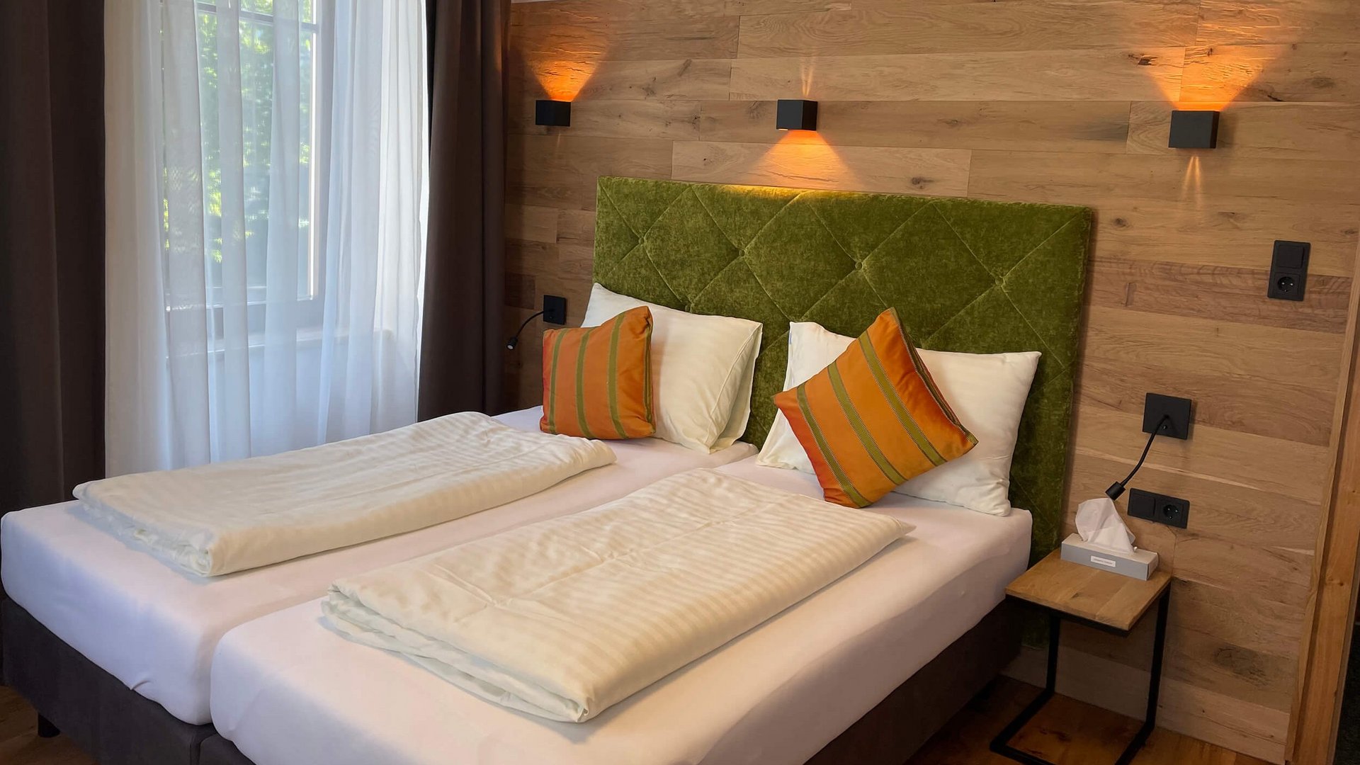 Modern bedroom with two single beds, green headboard, and wooden paneling