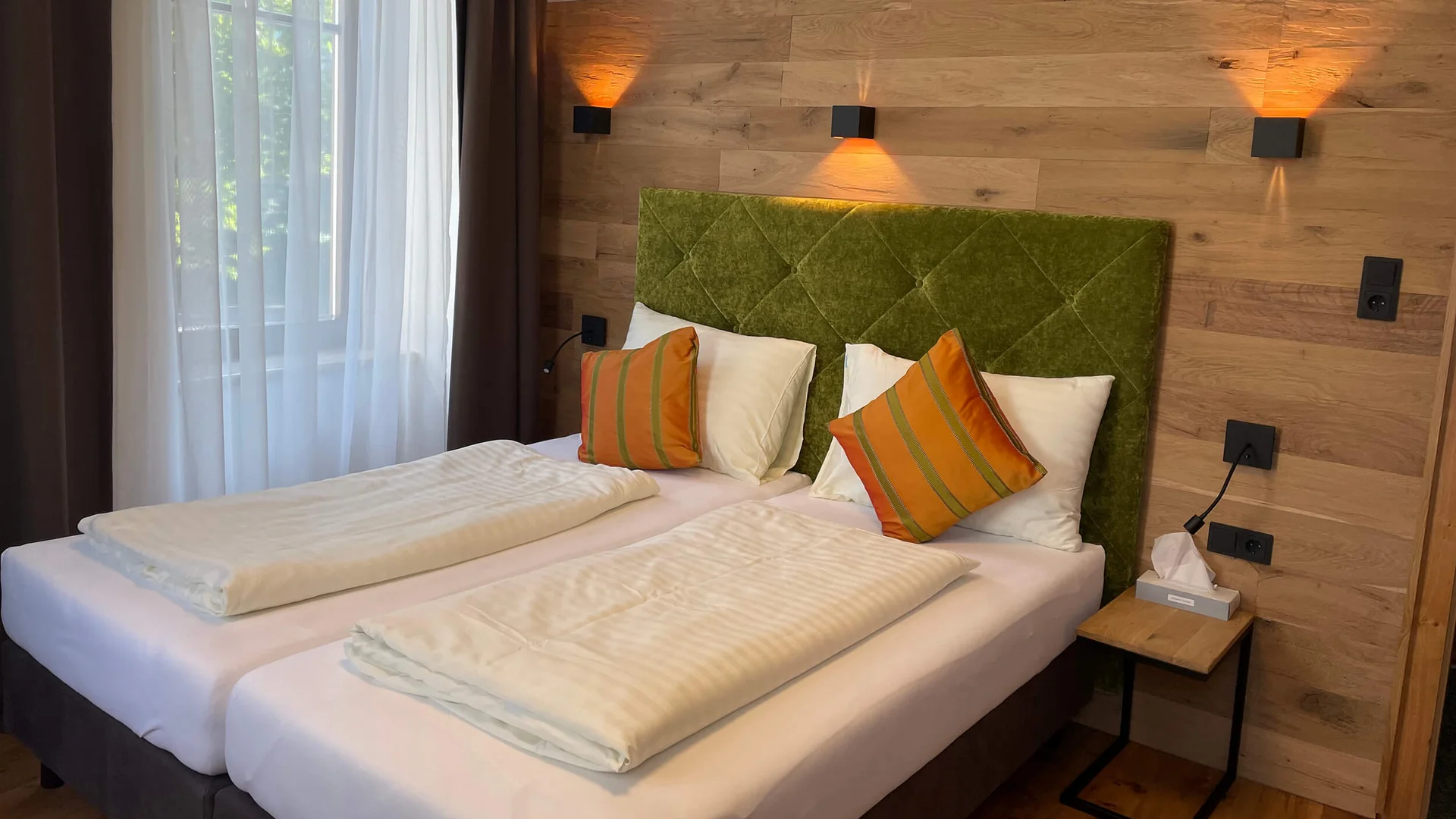 Modernes Schlafzimmer mit zwei Einzelbetten, grünem Kopfteil und Holzverkleidung