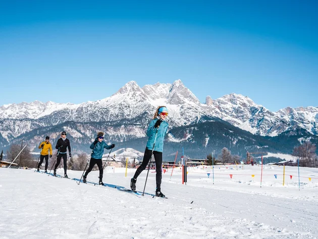 Gruppe beim Langlaufen vor schneebedeckten Bergen unter blauem Himmel