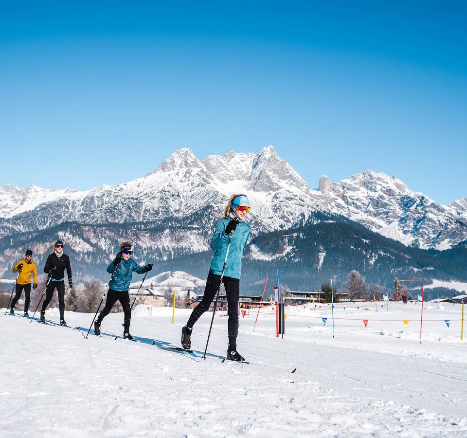 Gruppe beim Langlaufen vor schneebedeckten Bergen unter blauem Himmel