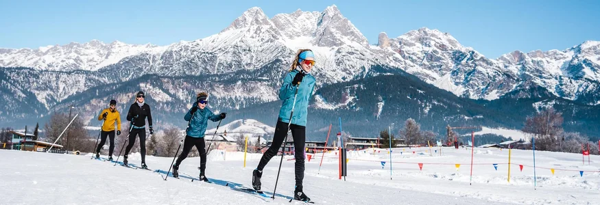 Gruppe beim Langlaufen vor schneebedeckten Bergen unter blauem Himmel