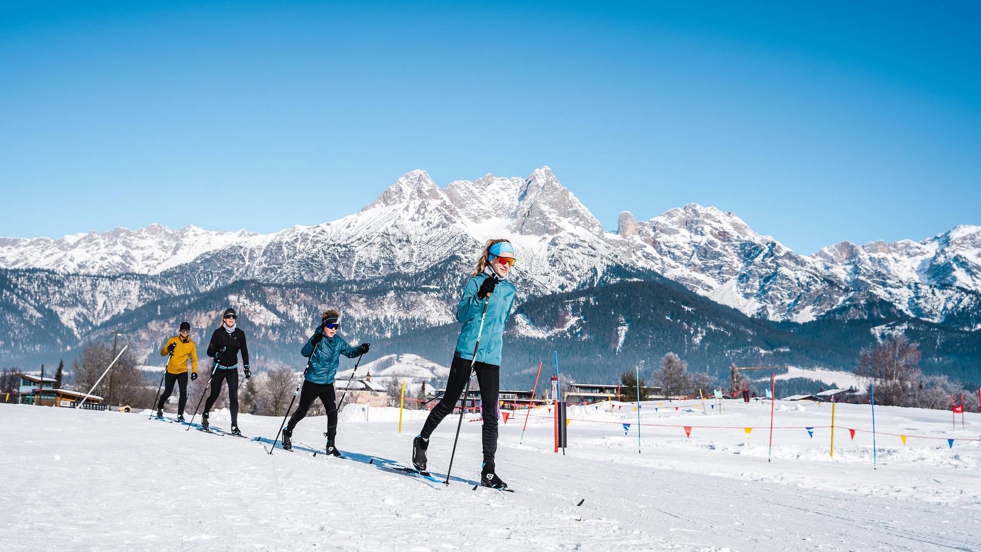 Gruppe beim Langlaufen vor schneebedeckten Bergen unter blauem Himmel
