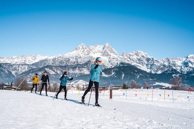 Gruppe beim Langlaufen vor schneebedeckten Bergen unter blauem Himmel