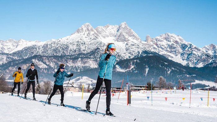 Gruppe beim Langlaufen vor schneebedeckten Bergen unter blauem Himmel