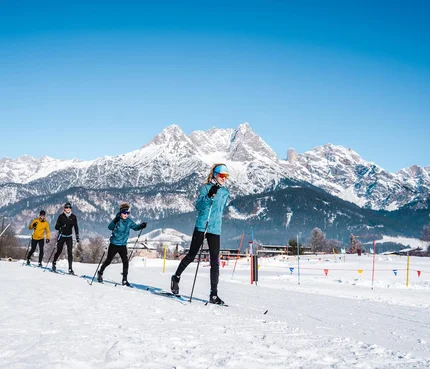 Gruppe beim Langlaufen vor schneebedeckten Bergen unter blauem Himmel