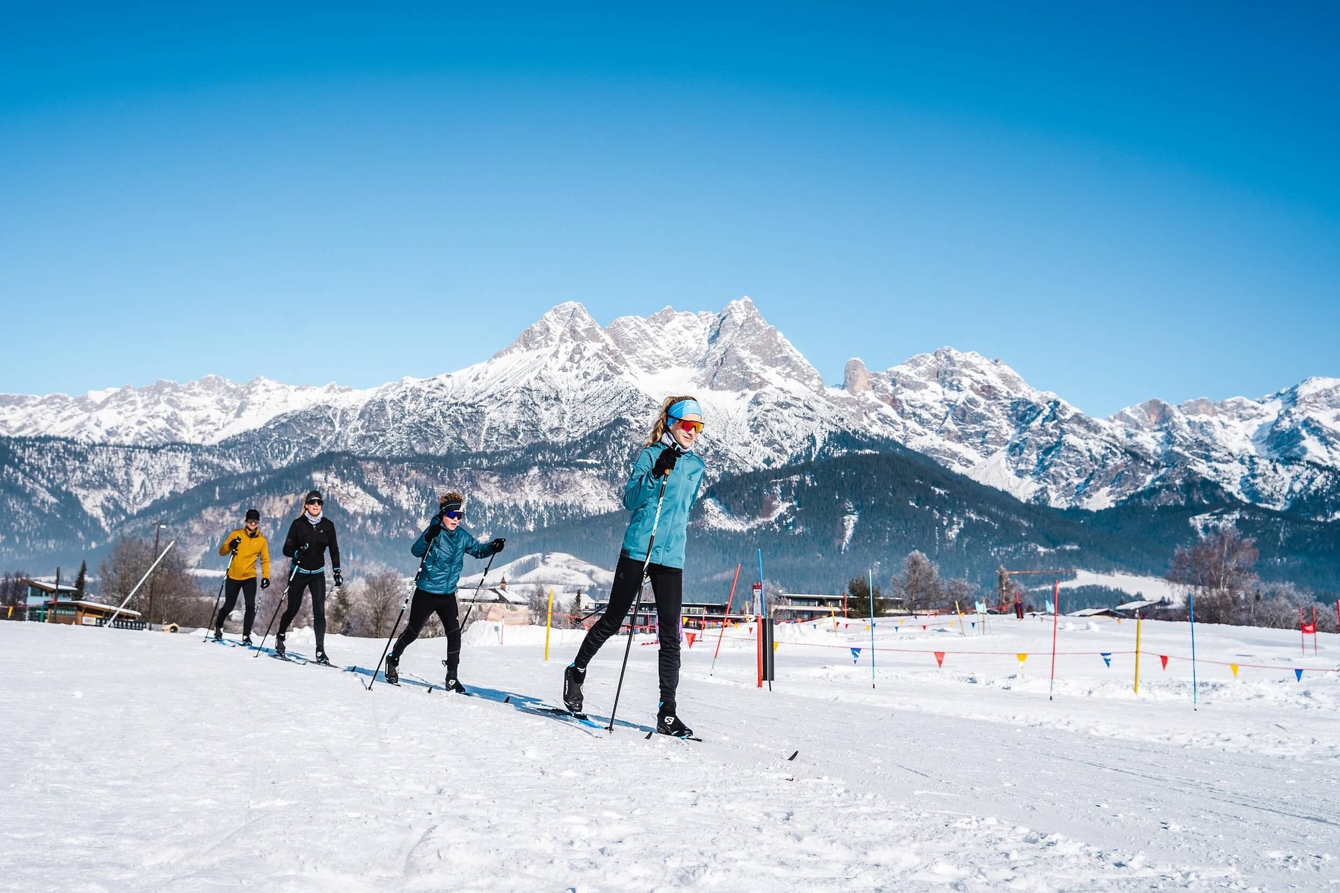 Gruppe beim Langlaufen vor schneebedeckten Bergen unter blauem Himmel