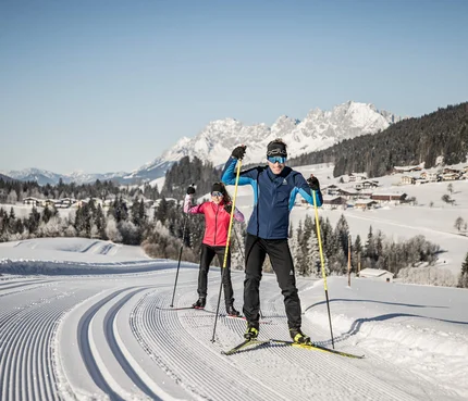 Zwei Menschen beim Langlaufen auf einer präparierten Loipe im schneebedeckten Gebirge