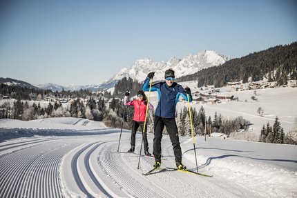 Zwei Menschen beim Langlaufen auf einer präparierten Loipe im schneebedeckten Gebirge