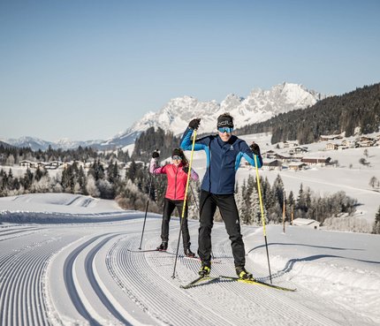Zwei Menschen beim Langlaufen auf einer präparierten Loipe im schneebedeckten Gebirge