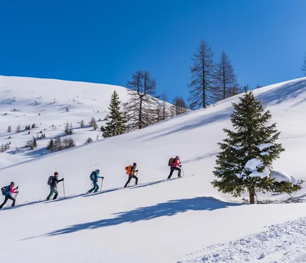 Fünf Menschen beim Aufstieg im Tiefschnee auf verschneitem Berg unter blauem Himmel