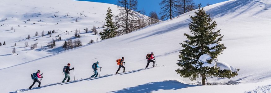 Five people hiking uphill on snowy mountain with clear blue sky