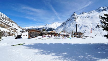 Schneebedeckte Skihütte in den Bergen mit Skiausrüstung und blauem Himmel
