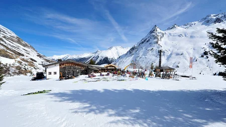 Schneebedeckte Skihütte in den Bergen mit Skiausrüstung und blauem Himmel