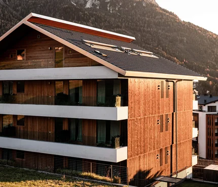 Modernes Holzhaus vor schneebedeckten Bergen im Sonnenlicht
