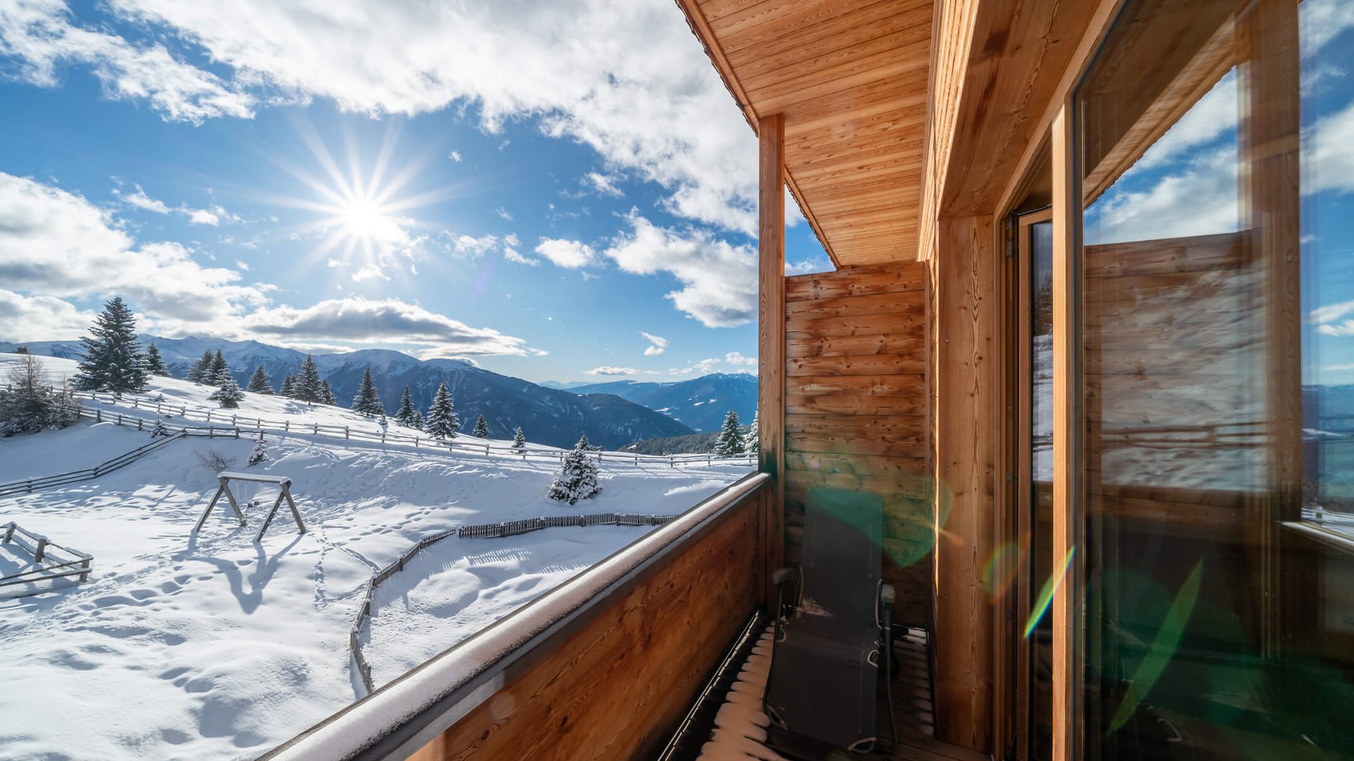 Balkon mit Liegestuhl und schneebedeckter Berglandschaft bei Sonnenschein