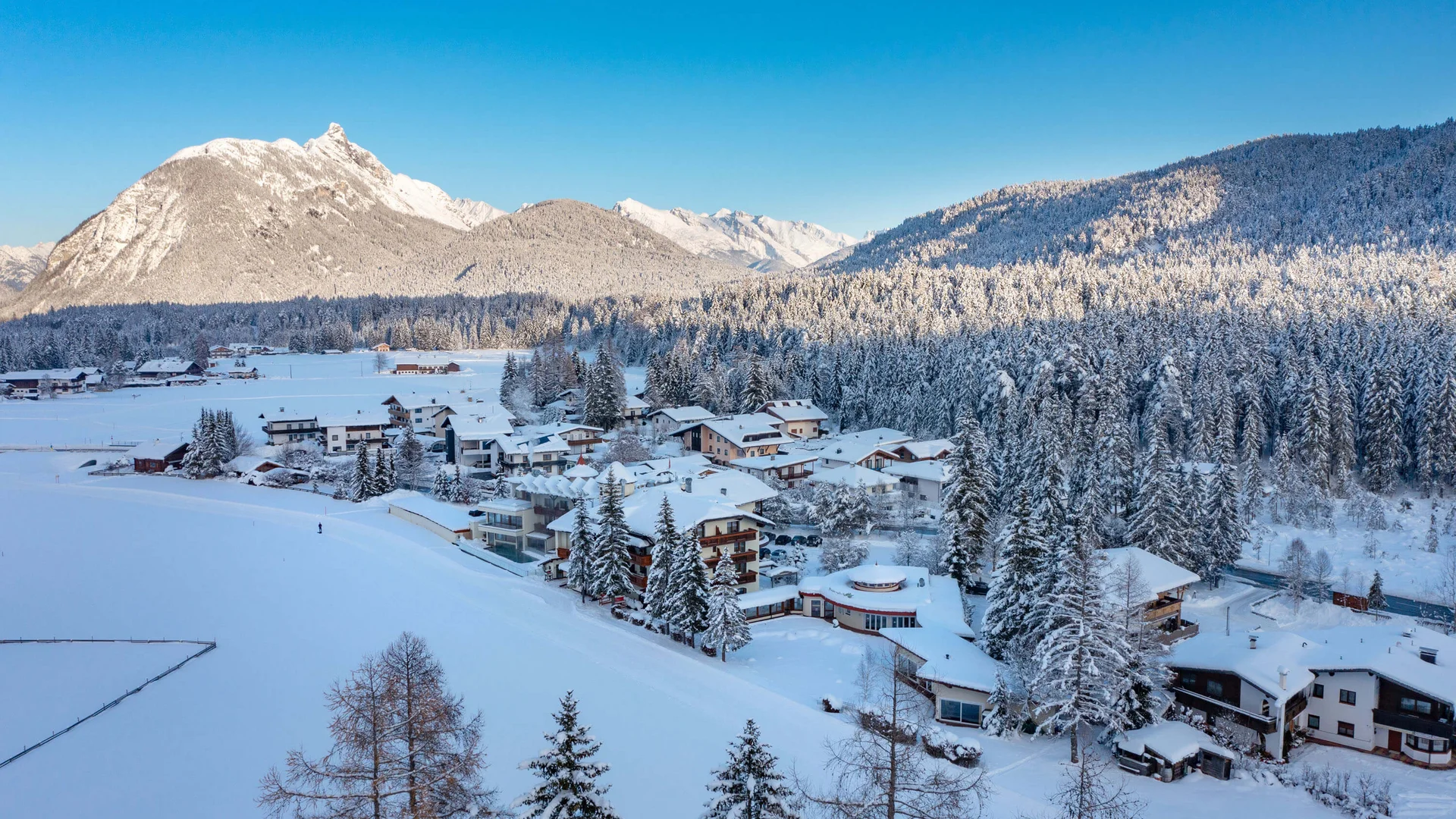 Langlaufopening in Leutasch © Region Seefeld - Hannes Dabernig Verschneites Bergdorf mit Wäldern und schneebedeckten Gipfeln unter blauem Himmel