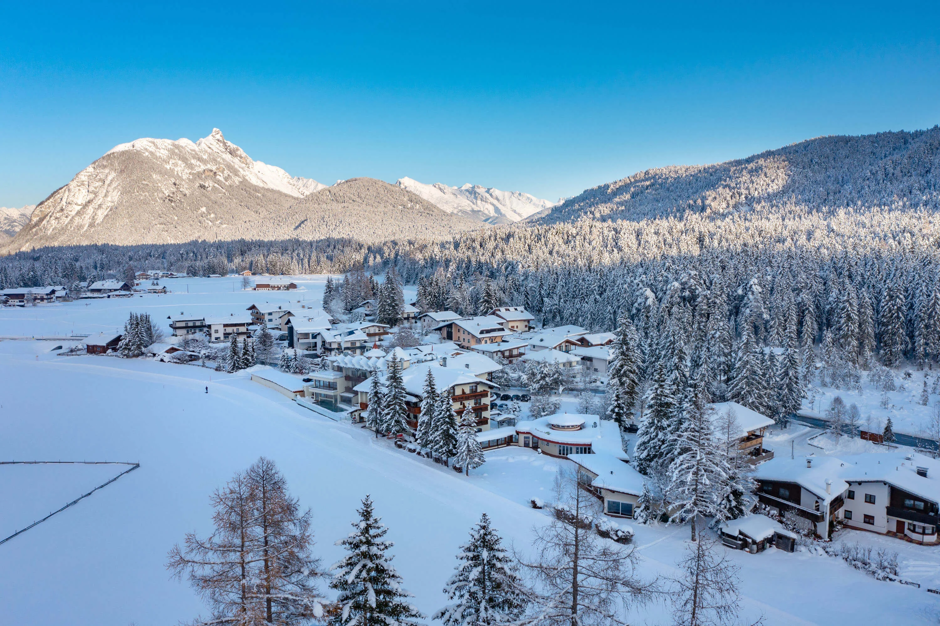 Langlaufopening in Leutasch © Region Seefeld - Hannes Dabernig Verschneites Bergdorf mit Wäldern und schneebedeckten Gipfeln unter blauem Himmel